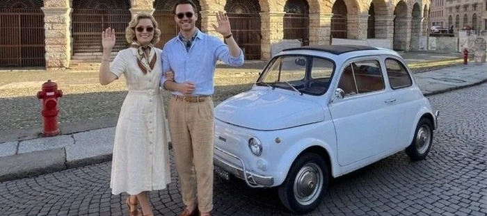 Una coppia in piedi accanto a una Fiat 500 azzurra davanti all'Arena di Verona